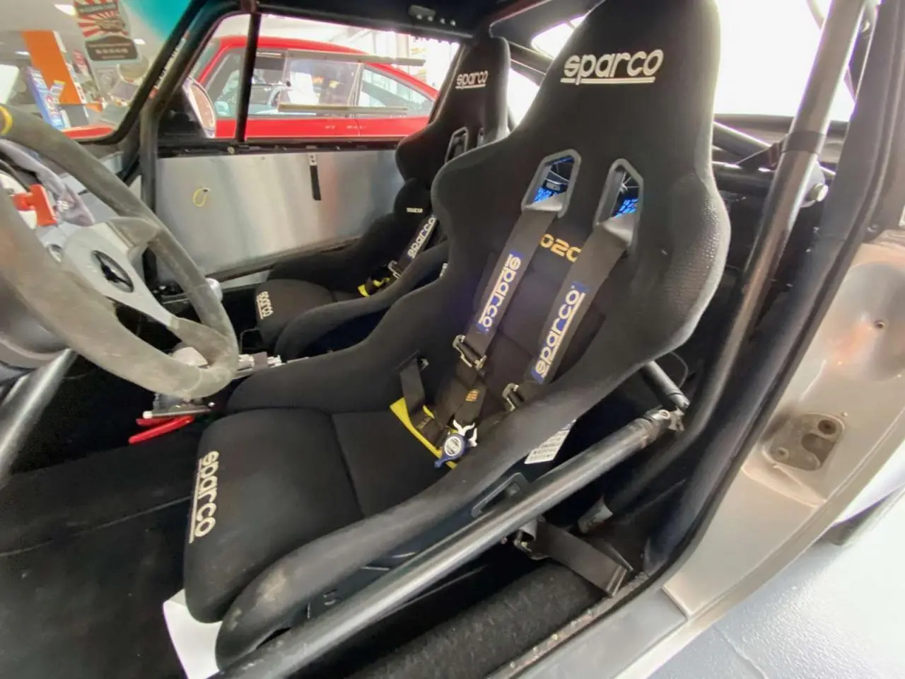 Intérieur de Porsche 911 3.0 SC gris, vue côté conducteur, sièges baquets Sparco avec harnais et arceau tubulaire.
