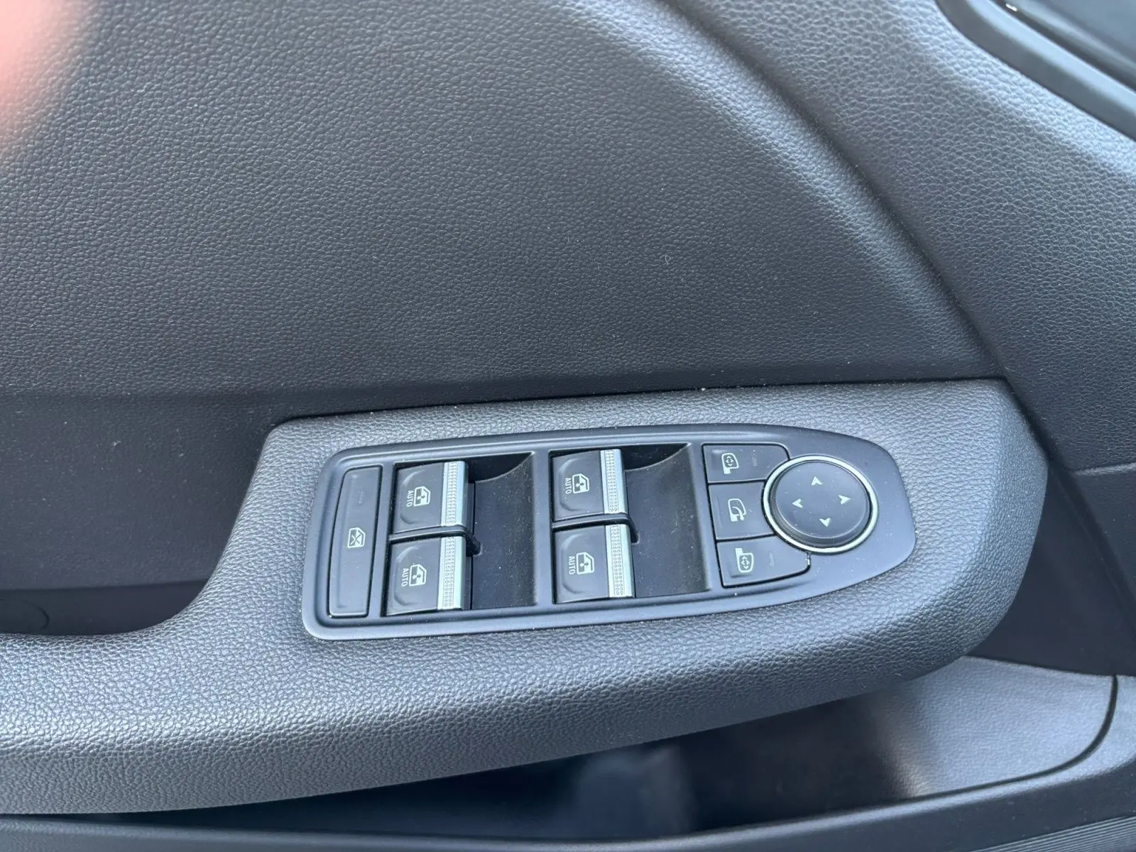 Gros plan sur les commandes des vitres électriques et des rétroviseurs sur la porte côté conducteur d'une Renault Clio gris foncé.