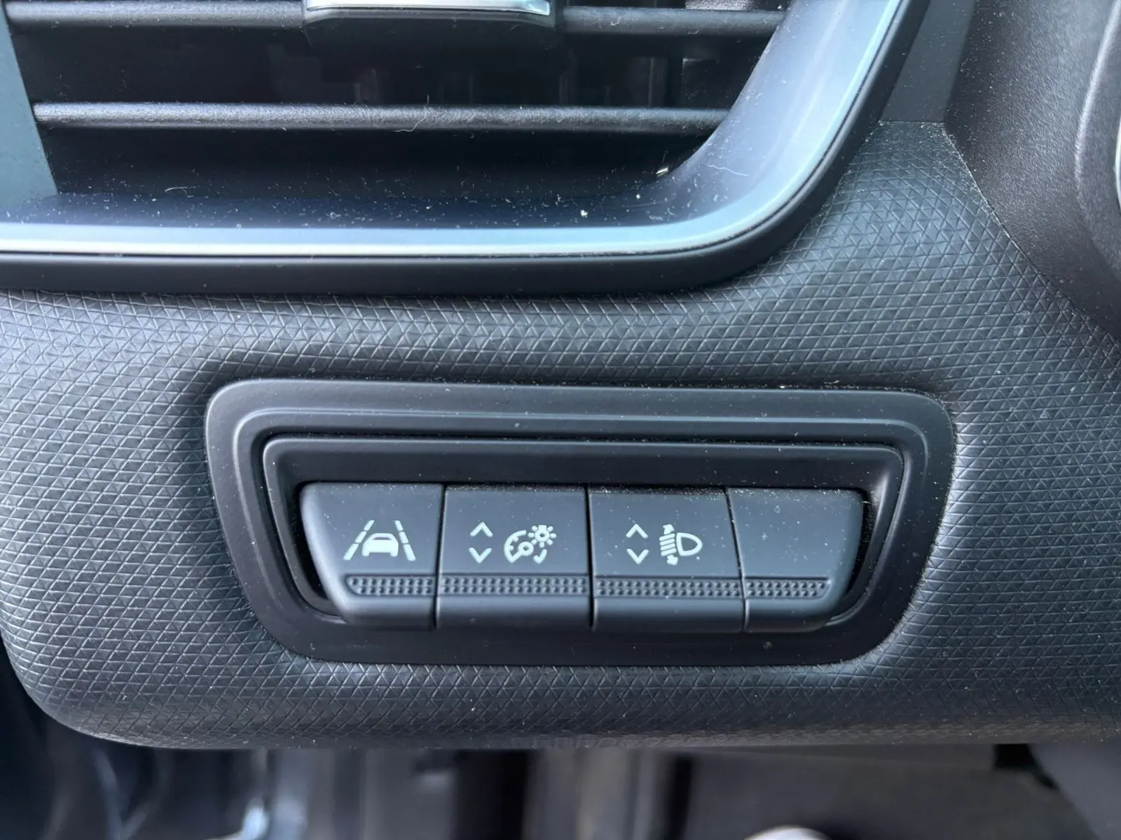 Gros plan sur les commandes d'aide à la conduite et réglage des phares dans l'habitacle d'une Renault Clio gris foncé 2021.