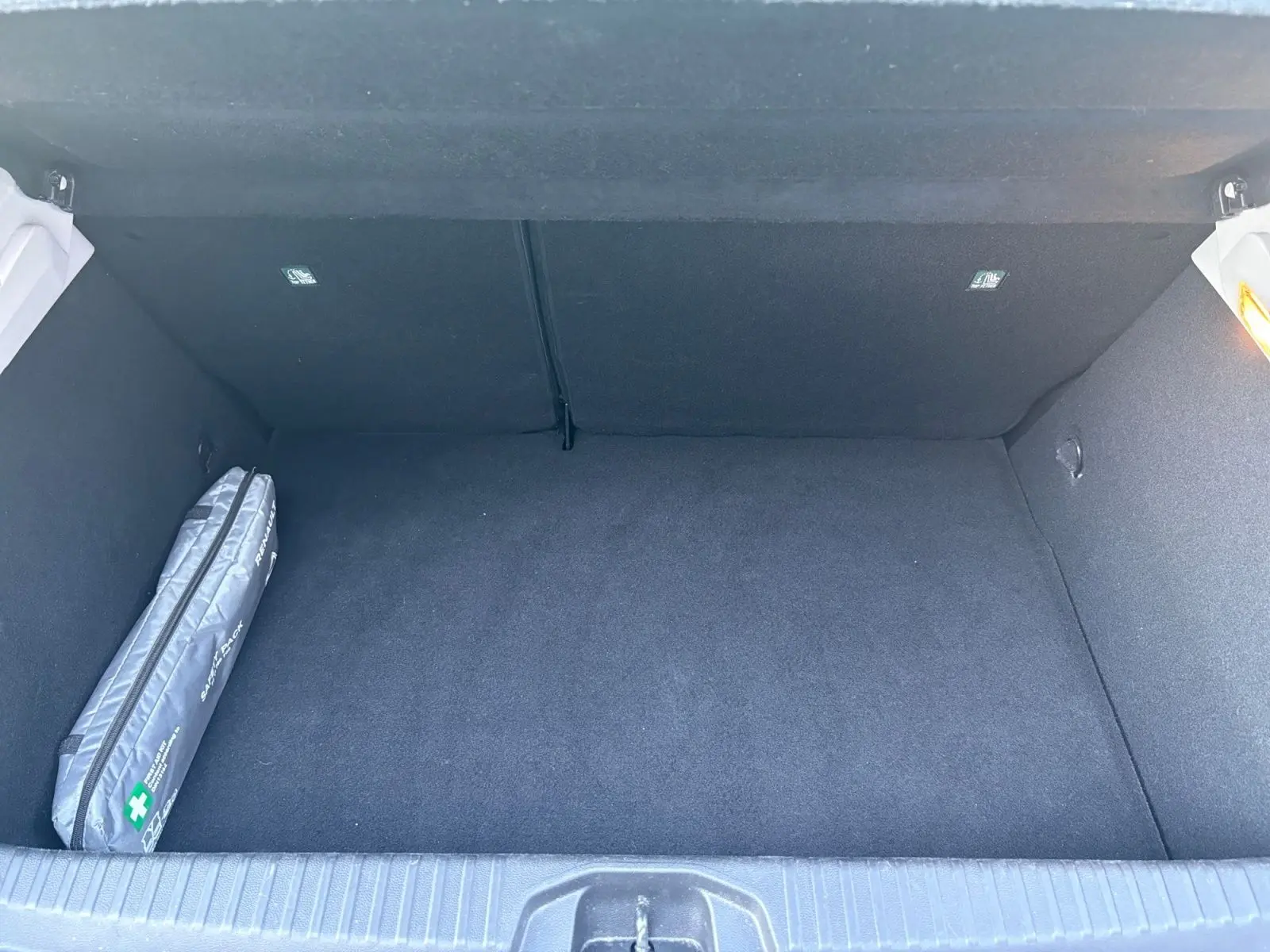 Coffre ouvert de la Renault Clio 1.6 E-TECH Business gris foncé, montrant un espace vide avec trousse de secours à gauche.