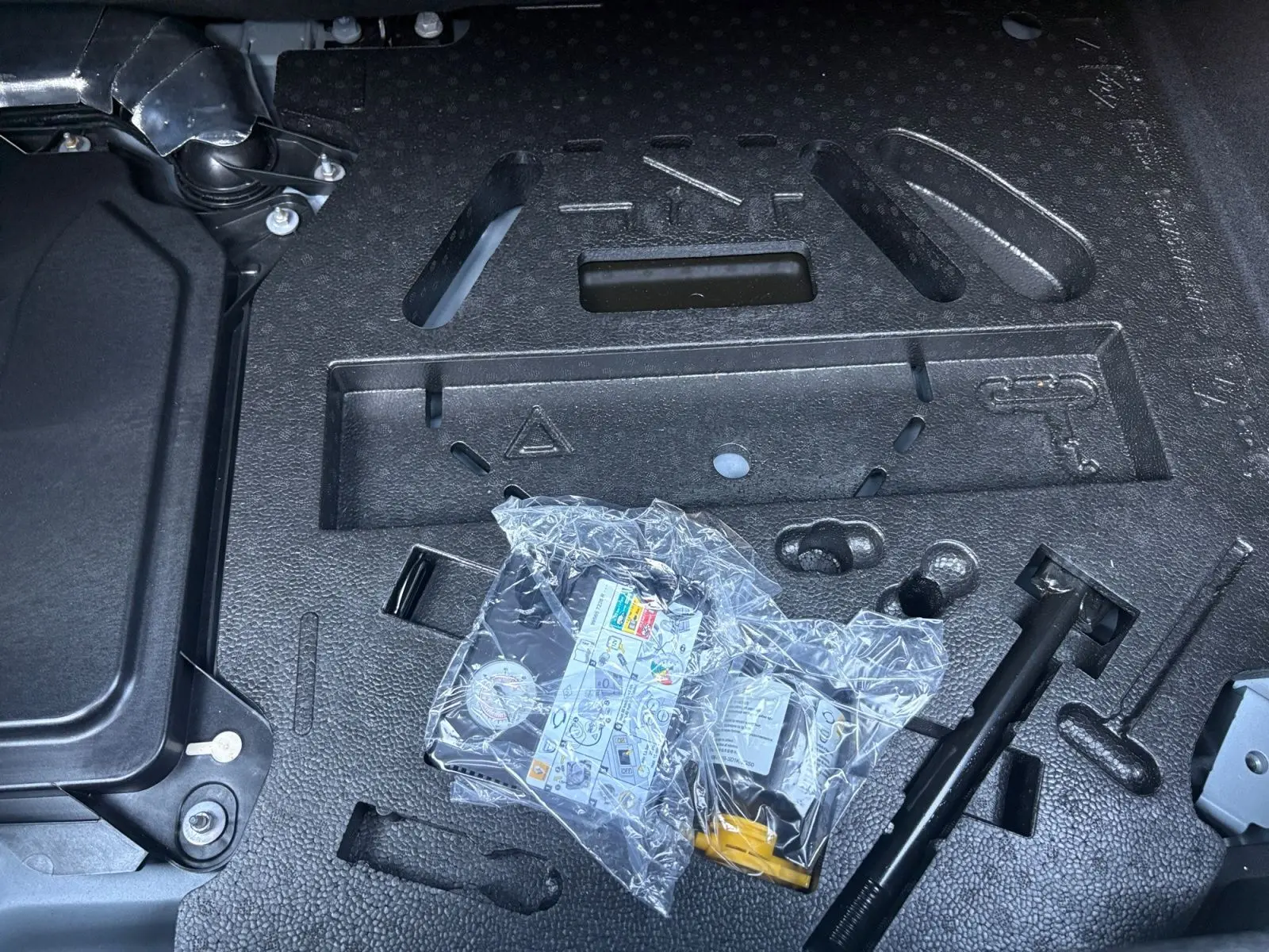 Gros plan sur le kit anti-crevaison dans le coffre d’une Renault Clio 1.6 E-TECH gris foncé, année 2021.