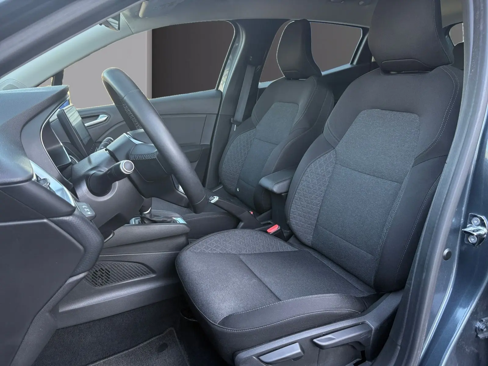 Vue intérieure côté conducteur de la Renault Clio 1.6 E-TECH Business 2021, sièges tissu gris foncé et tableau de bord moderne.