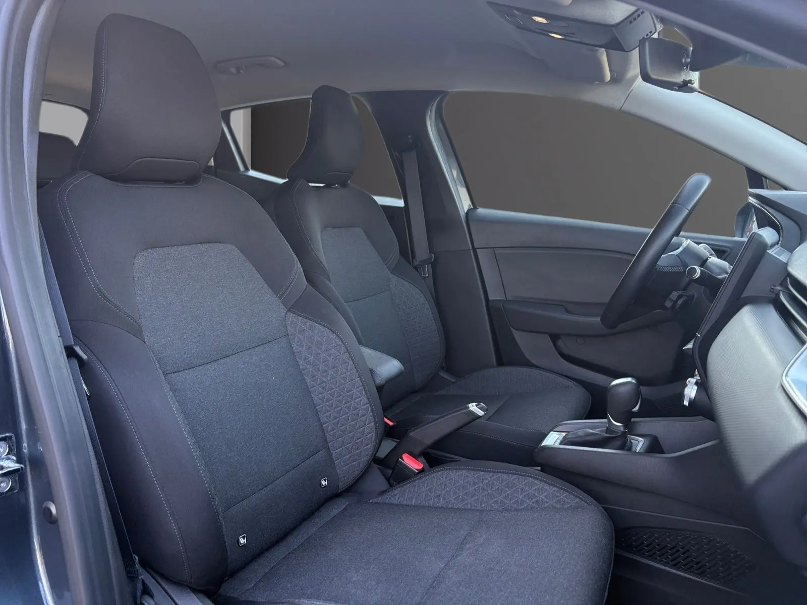 Vue intérieure côté conducteur de la Renault Clio 1.6 E-TECH Business 2021, sièges tissu gris foncé et tableau de bord moderne.