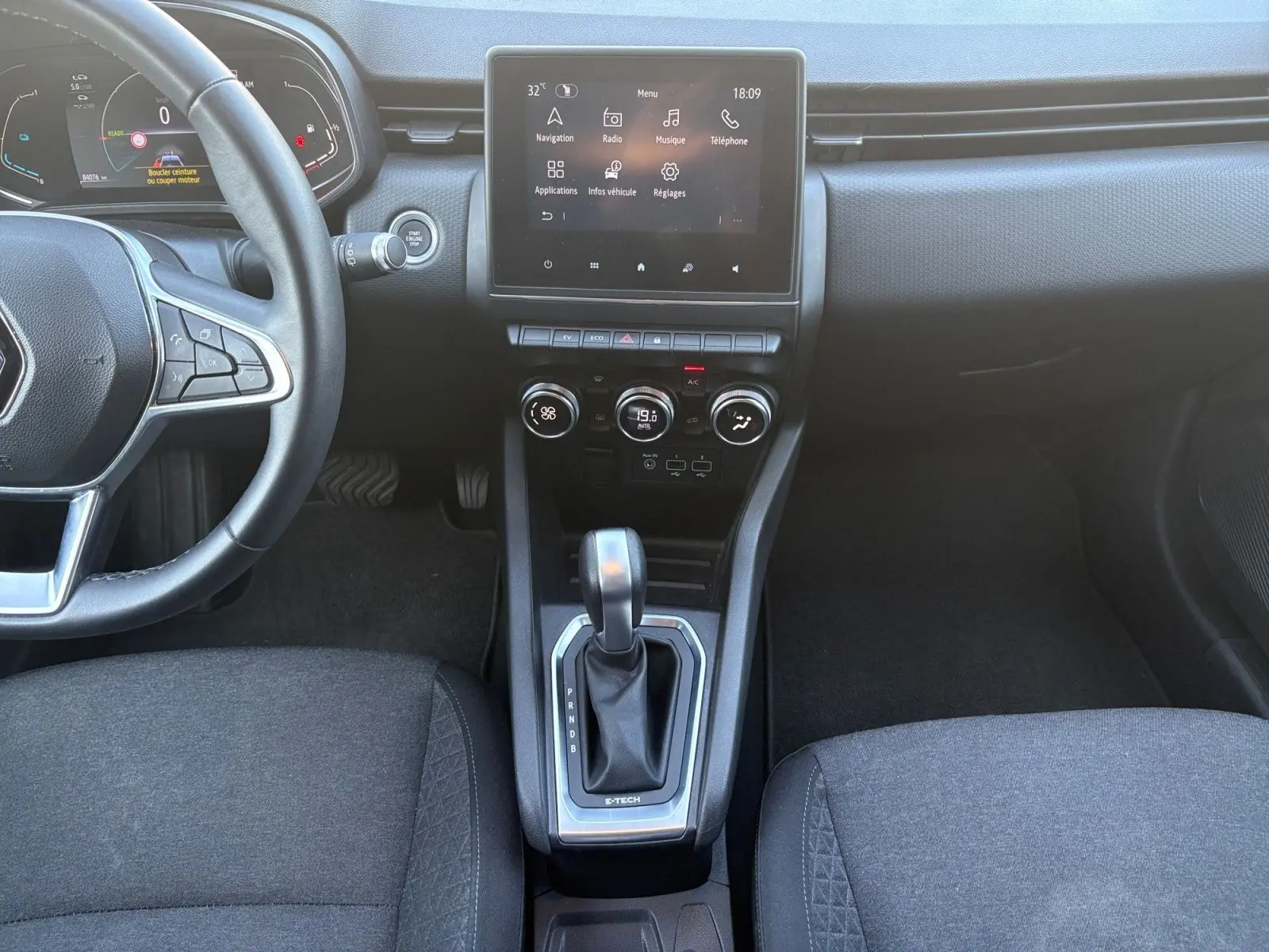Vue intérieure centrée sur la console centrale et levier de vitesse de la Renault Clio 1.6 E-TECH Business gris foncé avec écran tactile.