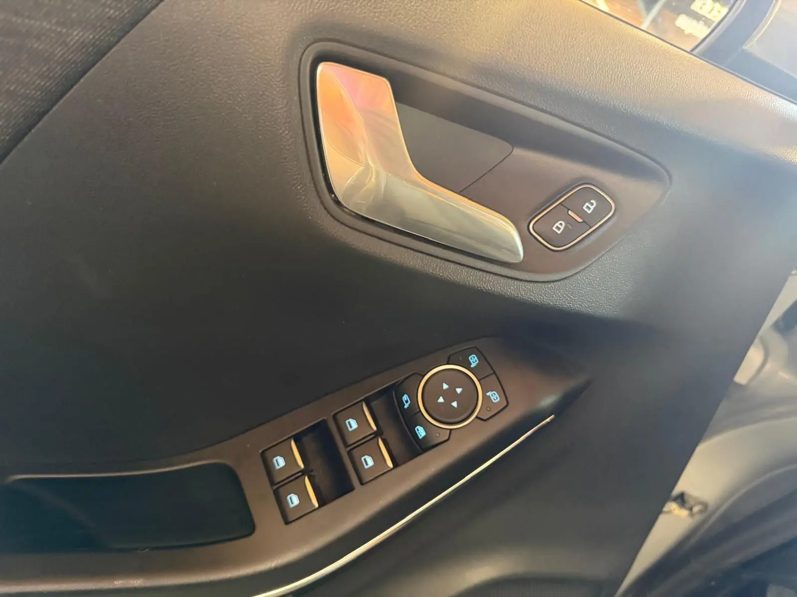 Gros plan sur la porte avant gauche du Ford Puma gris, montrant la poignée chromée et les commandes électriques des vitres.