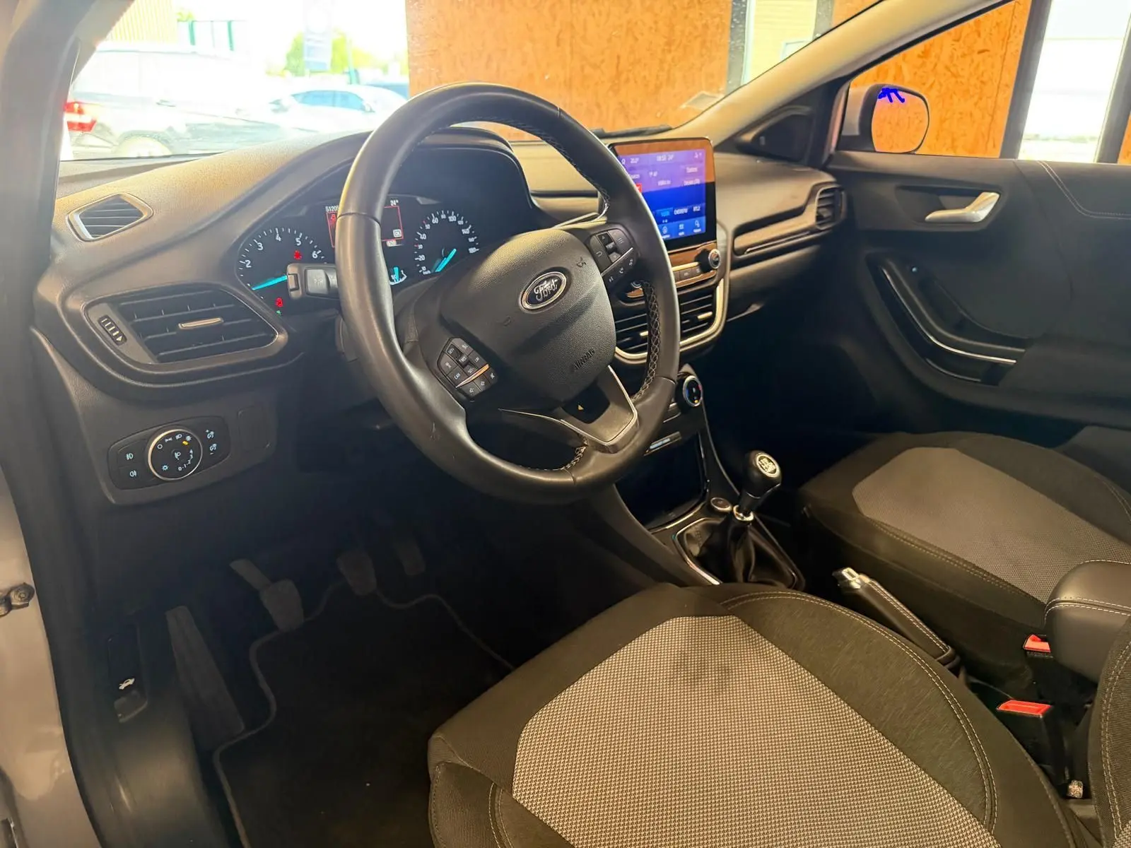 Vue intérieure côté conducteur du Ford Puma gris 2021, volant multifonction, tableau de bord digital et levier de vitesse manuel.