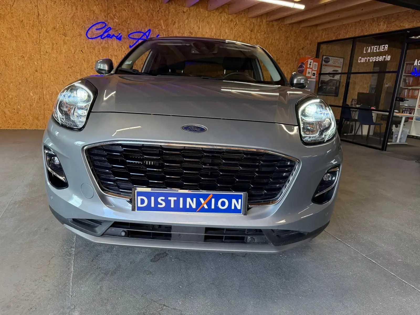 Vue avant rapprochée du Ford Puma gris 2021 avec calandre noire et phares allumés en intérieur showroom.