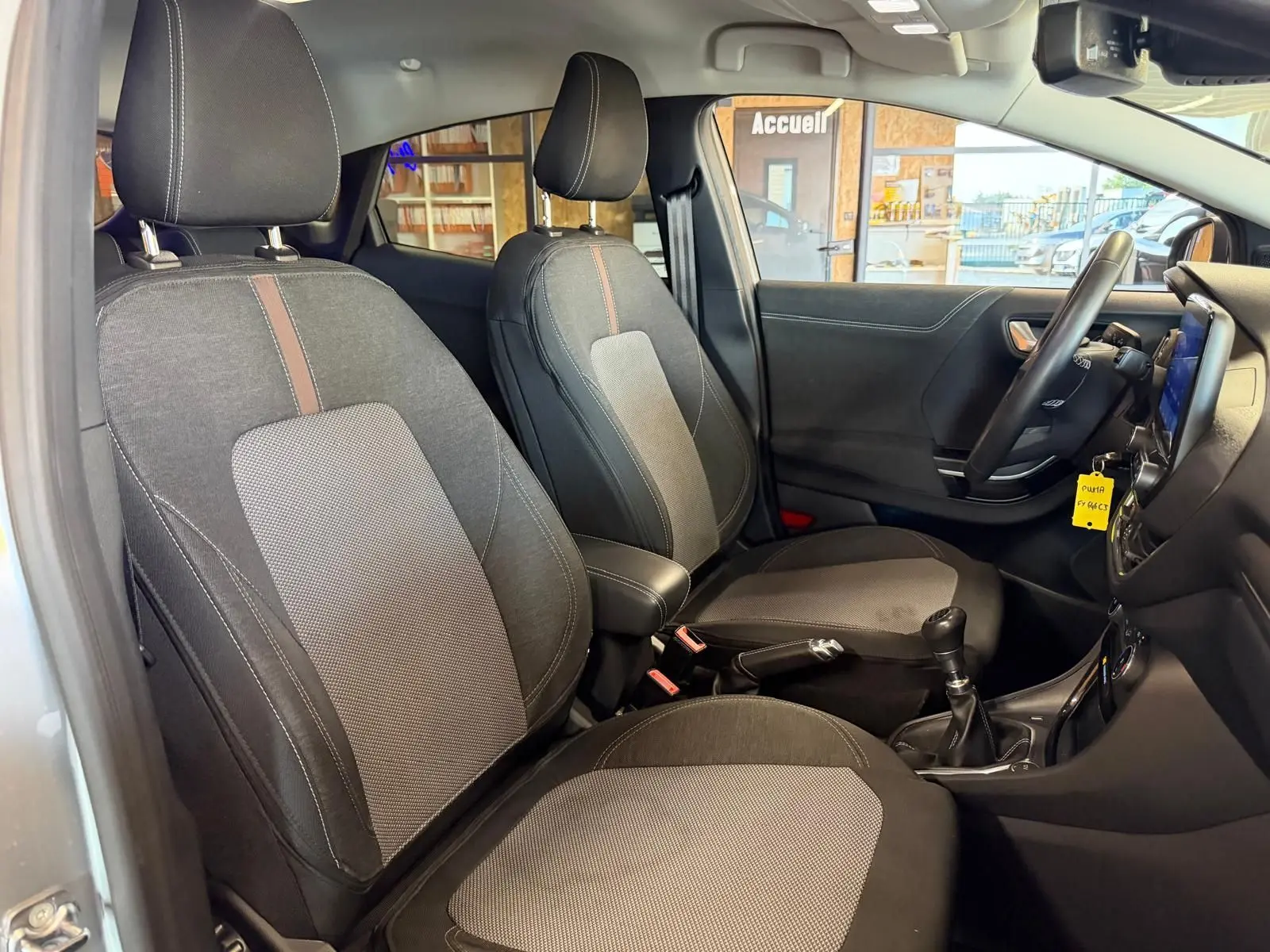 Vue intérieure côté conducteur du Ford Puma gris 2021, sièges tissu noir avec console centrale et levier de vitesses manuel.