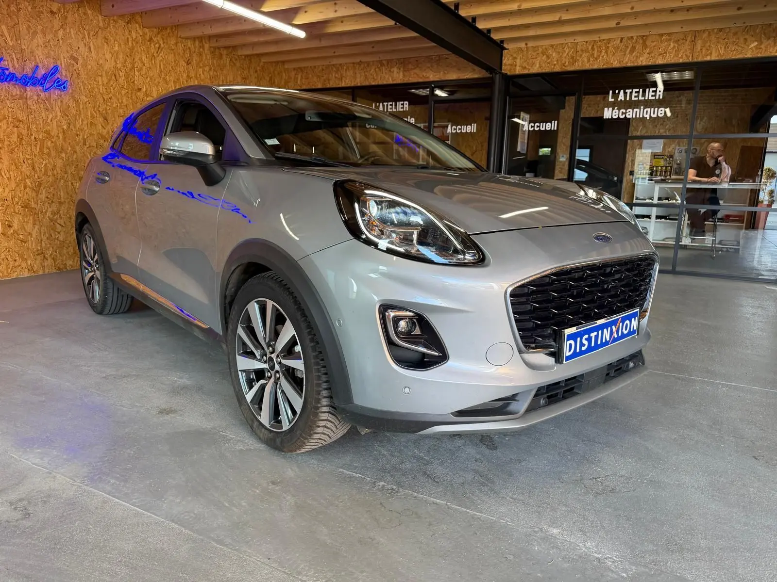 Ford Puma gris vue 3/4 avant droit dans un garage avec calandre noire et jantes alliage distinctives.