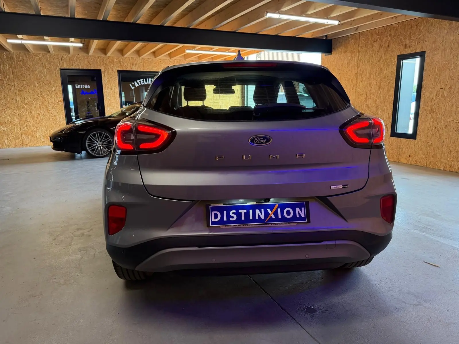Vue arrière d'une Ford Puma gris métallisé 2021, avec feux arrière allumés et plaque Distinxion visible.