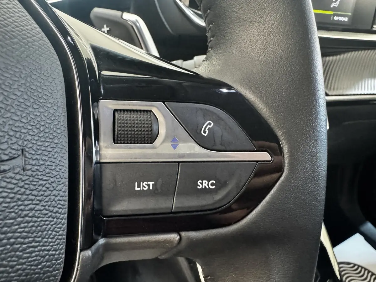 Gros plan sur les commandes gauche du volant cuir noir du Peugeot 2008 2022, boutons LIST, SRC et téléphone.
