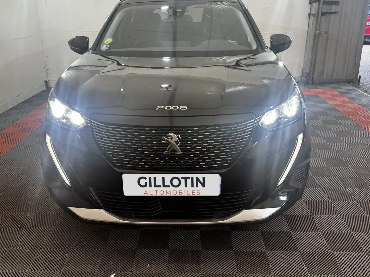Vue frontale d’un Peugeot 2008 noir avec phares LED allumés et calandre distinctive en intérieur showroom.