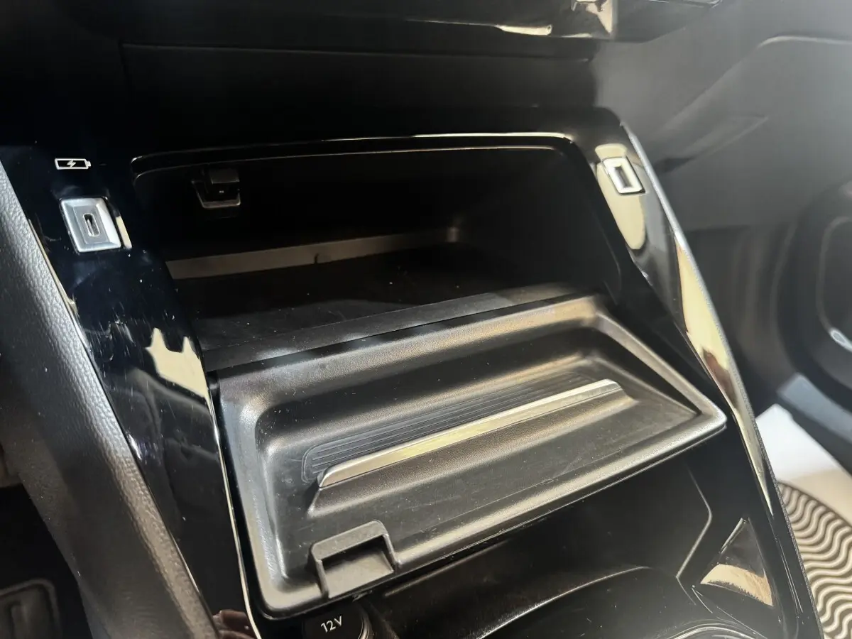 Gros plan sur la console centrale noire du Peugeot 2008 2022, montrant un rangement avec ports USB et prise 12V.