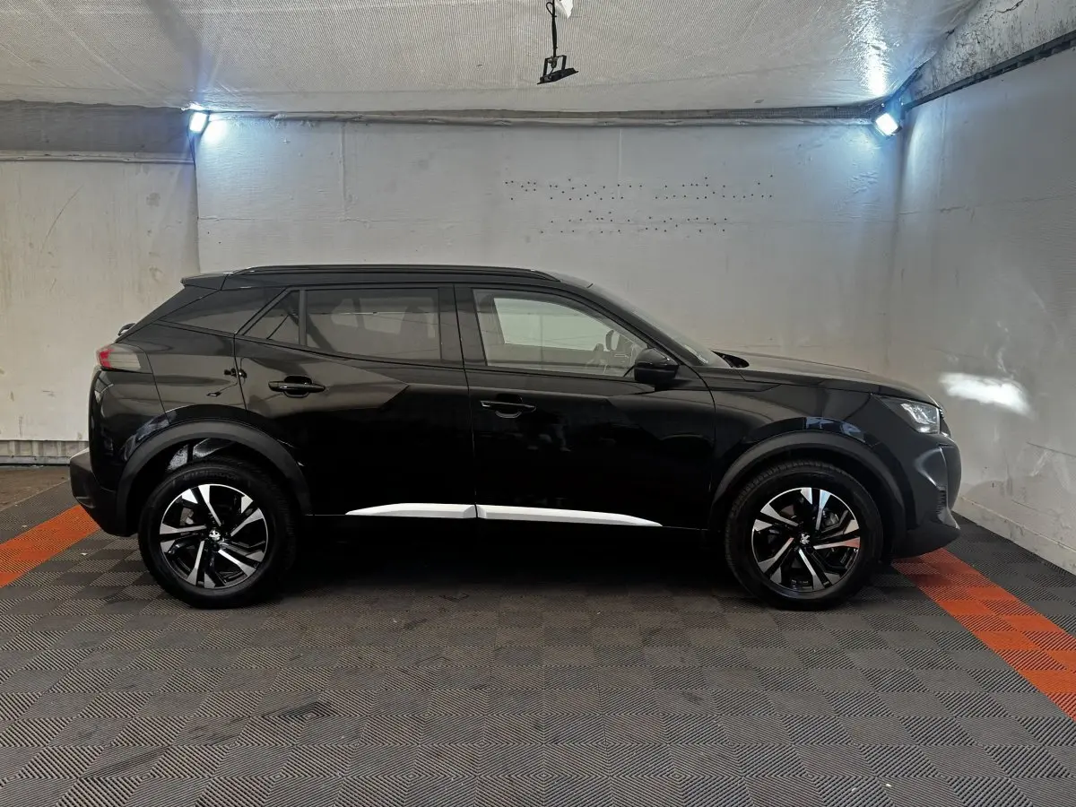 Profil côté gauche d’un Peugeot 2008 noir 2022 avec jantes alliage bicolores et barres de toit assorties.