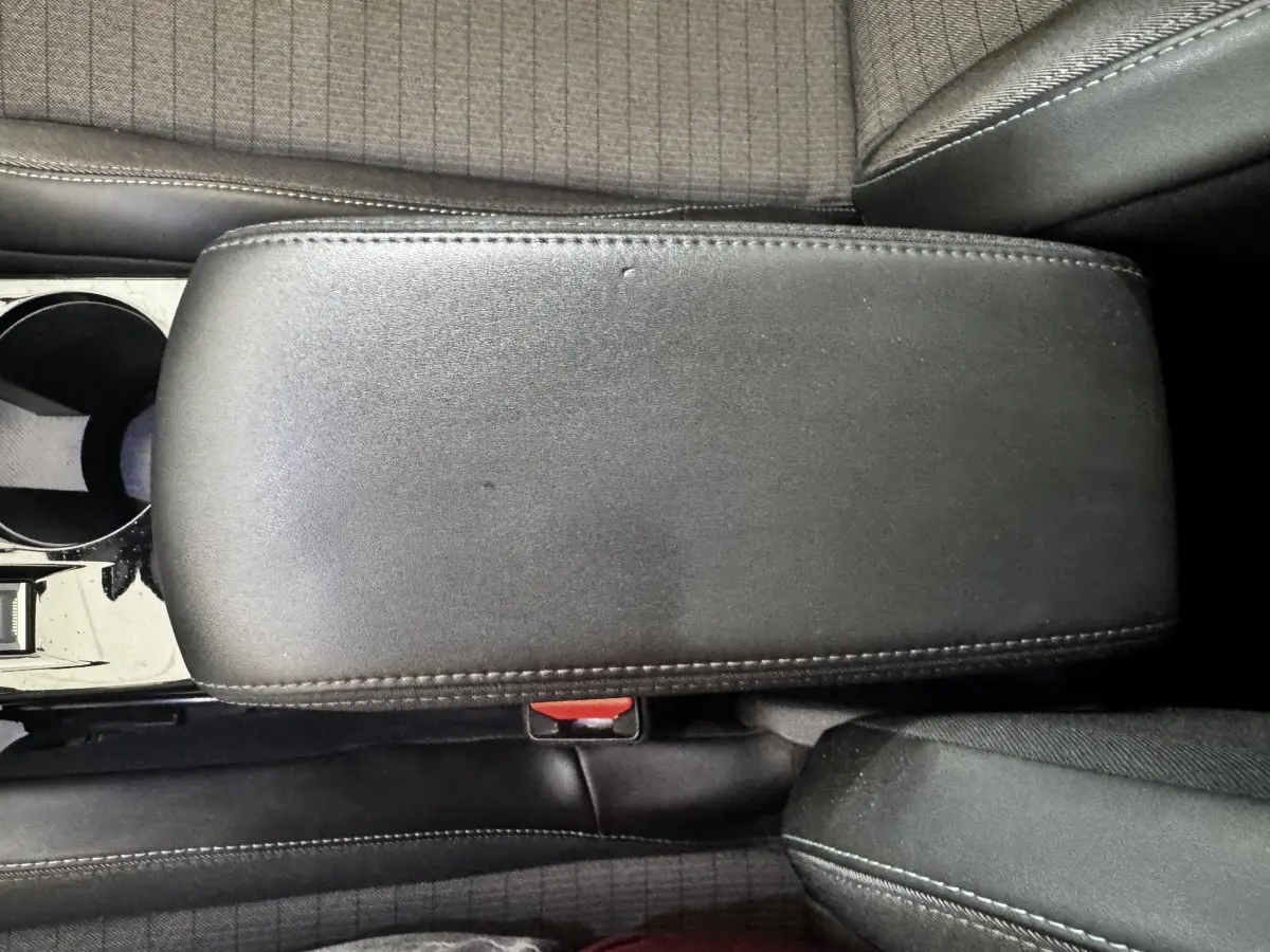 Vue rapprochée de l'accoudoir central en cuir noir et des sièges tissu gris foncé à motifs du Peugeot 2008 noir.