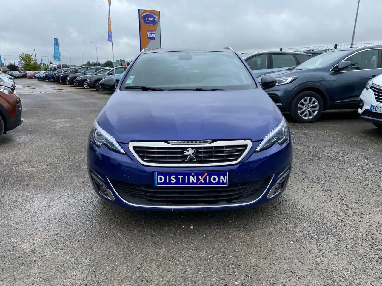 Vue frontale d'une Peugeot 308 SW GT Line bleu magnétique, avec calandre chromée et feux LED allumés.