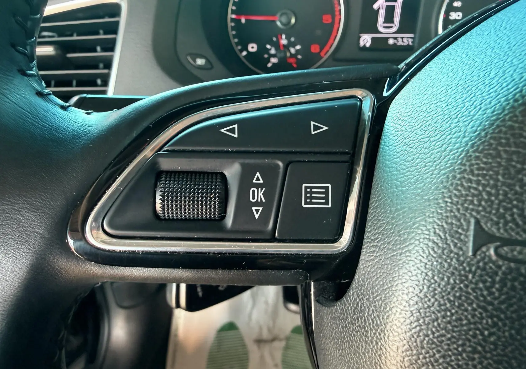 Gros plan sur les commandes gauche du volant noir de l'Audi Q3 2016 avec tableau de bord en arrière-plan.