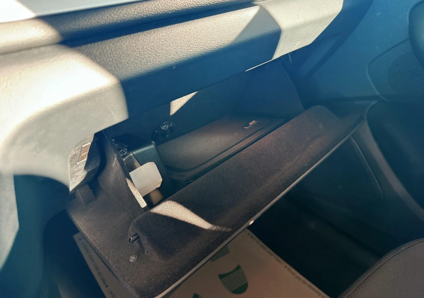 Vue intérieure du vide-poche ouvert côté passager de l'Audi Q3 noir, montrant un rangement avec un étui noir à l'intérieur.