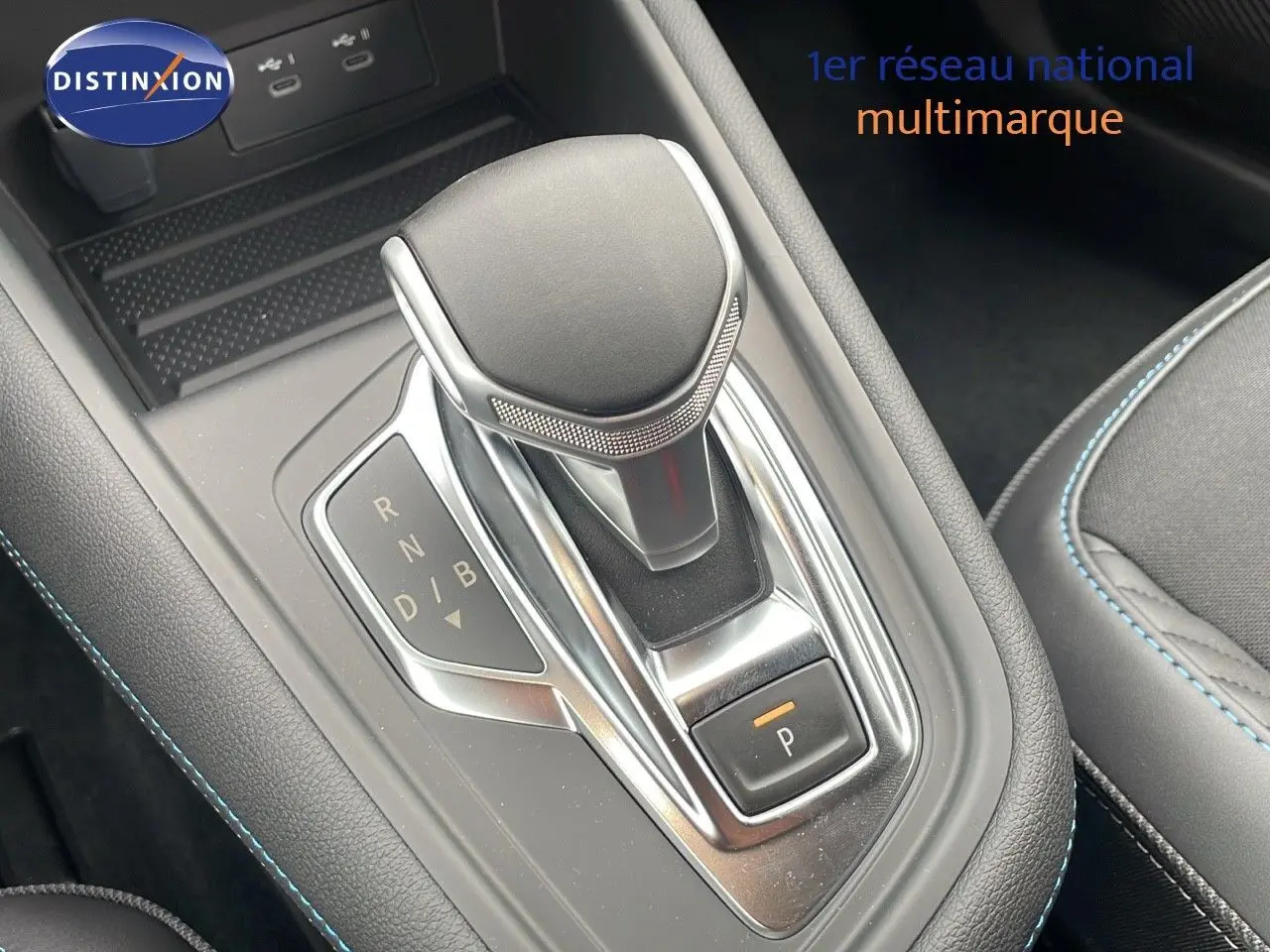 Le levier de vitesses automatique noir et chrome de la Renault Symbioz 2025, avec surpiqûres bleues visibles sur l'accoudoir.