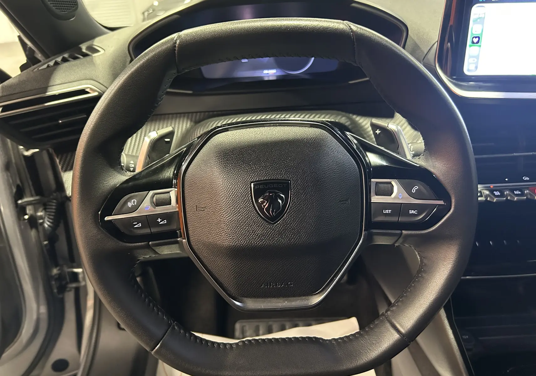 Gros plan sur le volant cuir noir du Peugeot 2008 II Ph.2 Allure Hybrid 145 avec commandes intégrées et tableau de bord numérique.