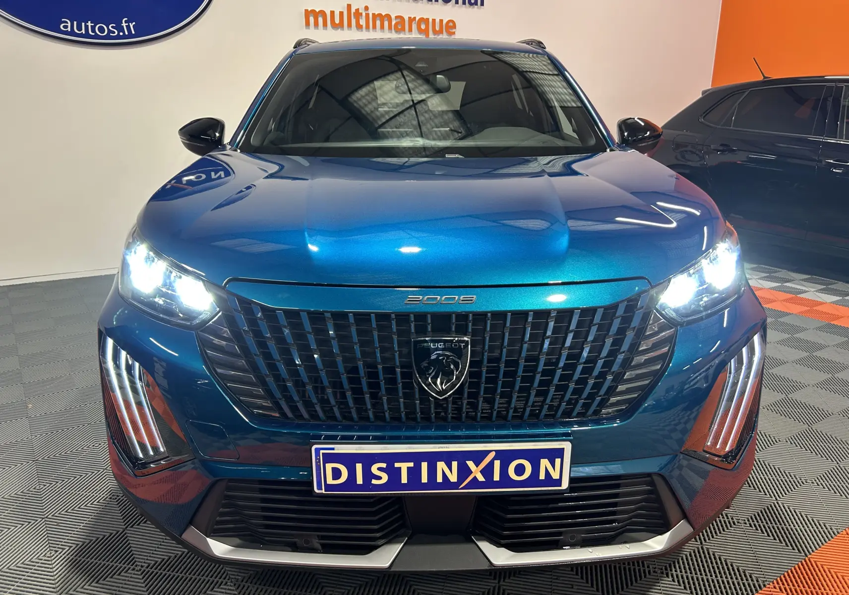 Vue avant d’un Peugeot 2008 bleu Obsession avec phares allumés et calandre noire distinctive en showroom.