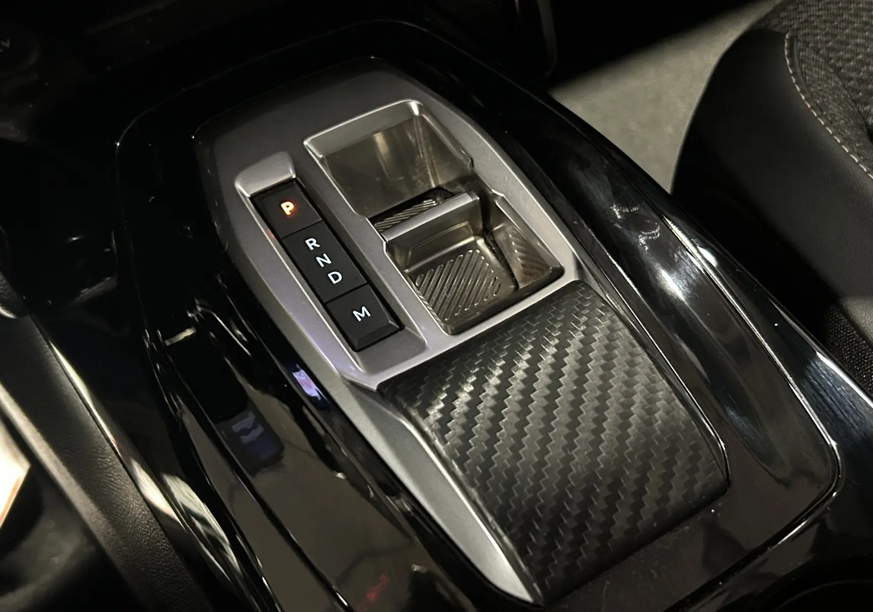 Gros plan sur la console centrale noire brillante avec levier de vitesses automatique et finition carbone dans un Peugeot 2008 Bleu Obsession.