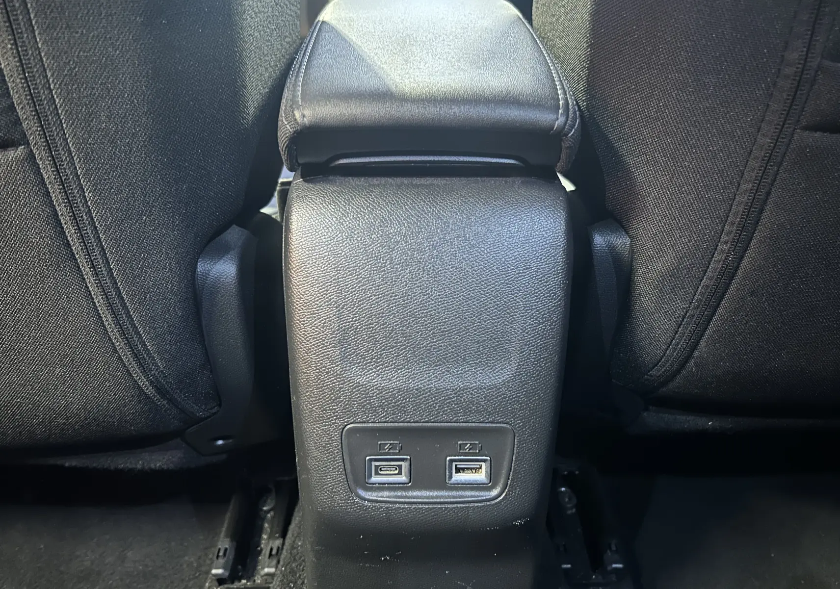 Vue rapprochée de la console centrale arrière noire du Peugeot 2008 bleu, avec ports USB visibles entre les sièges.