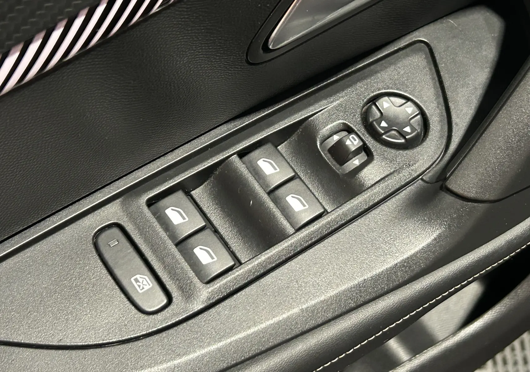 Gros plan sur les commandes de lève-vitres et réglage des rétroviseurs côté conducteur du Peugeot 2008 bleu Obsession.
