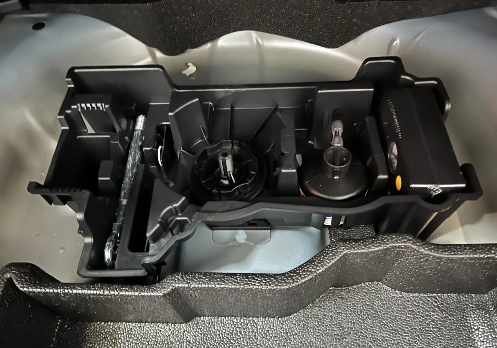 Vue rapprochée de l’espace de rangement sous coffre du Peugeot 2008 bleu, montrant les outils et accessoires intégrés.