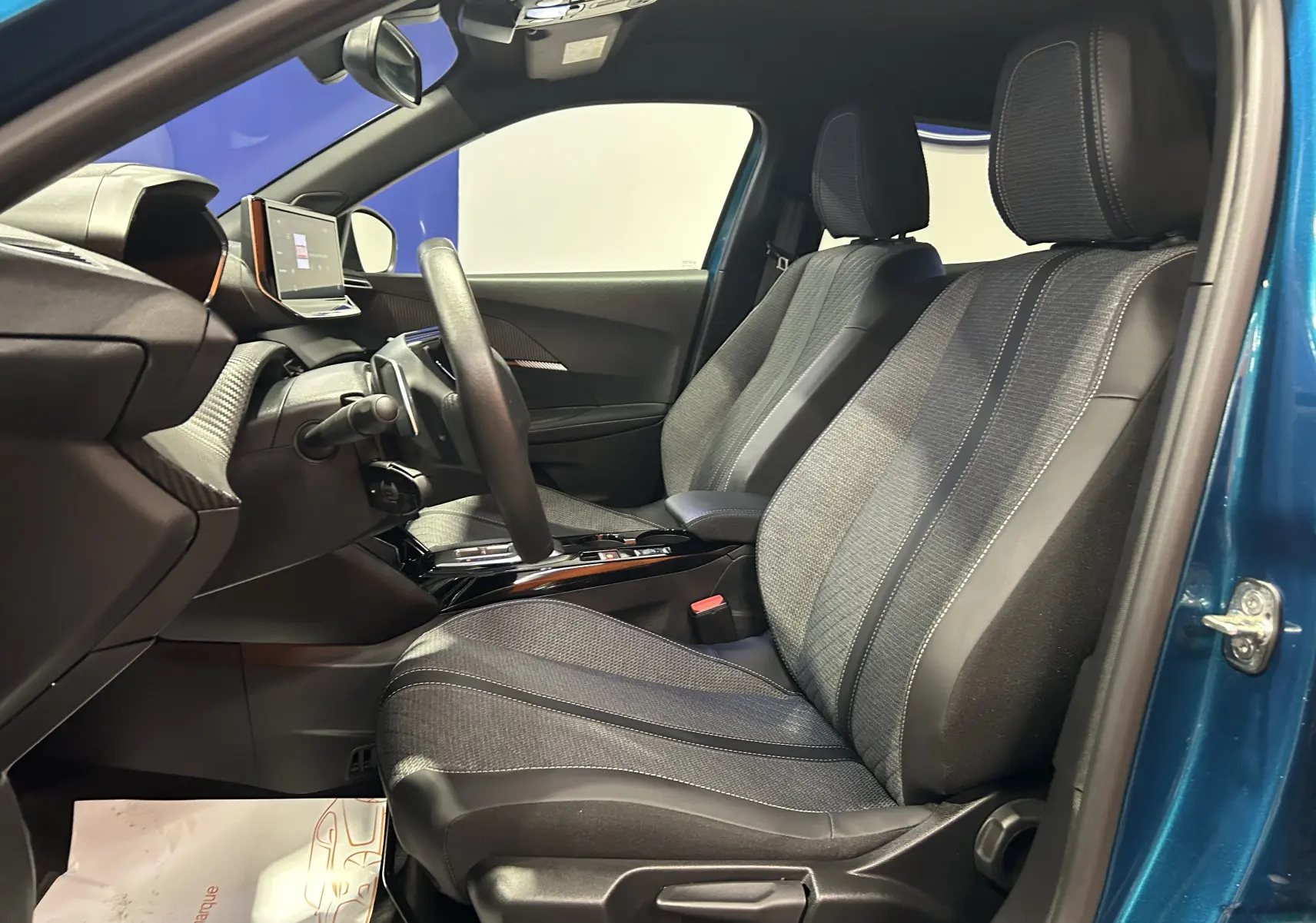 Vue intérieure côté conducteur du Peugeot 2008 bleu Obsession, sièges tissu et cuir avec tableau de bord moderne et écran tactile.