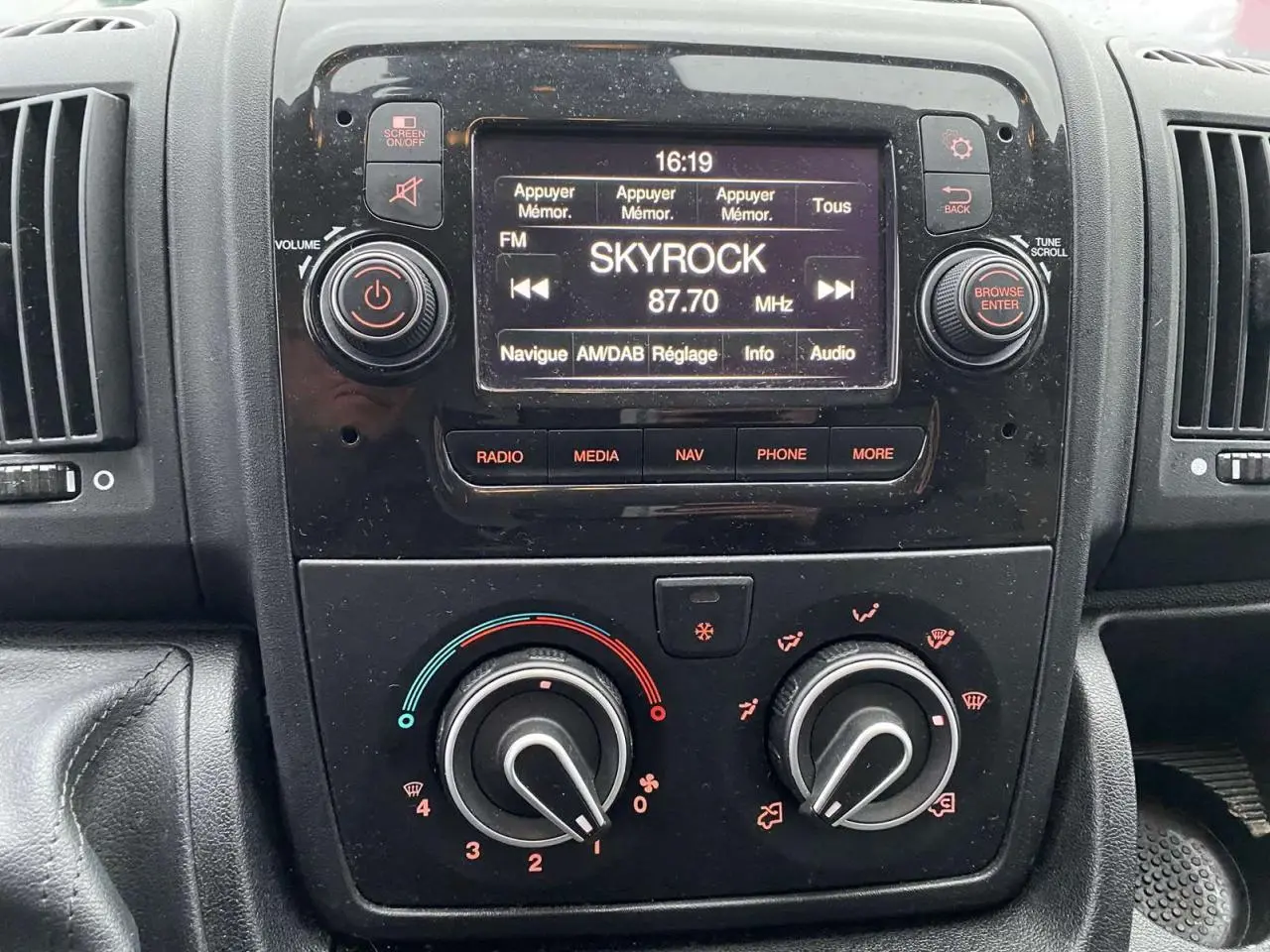 Vue rapprochée du tableau de bord noir de l'Opel Movano Fourgon blanc, avec écran radio affichant Skyrock 87.7 MHz.