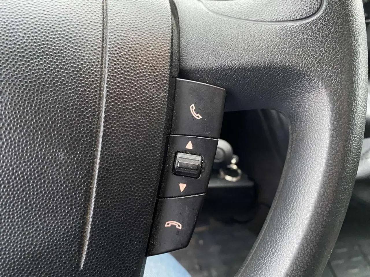 Gros plan sur les commandes de téléphone intégrées au volant noir d’un Opel Movano Fourgon blanc.