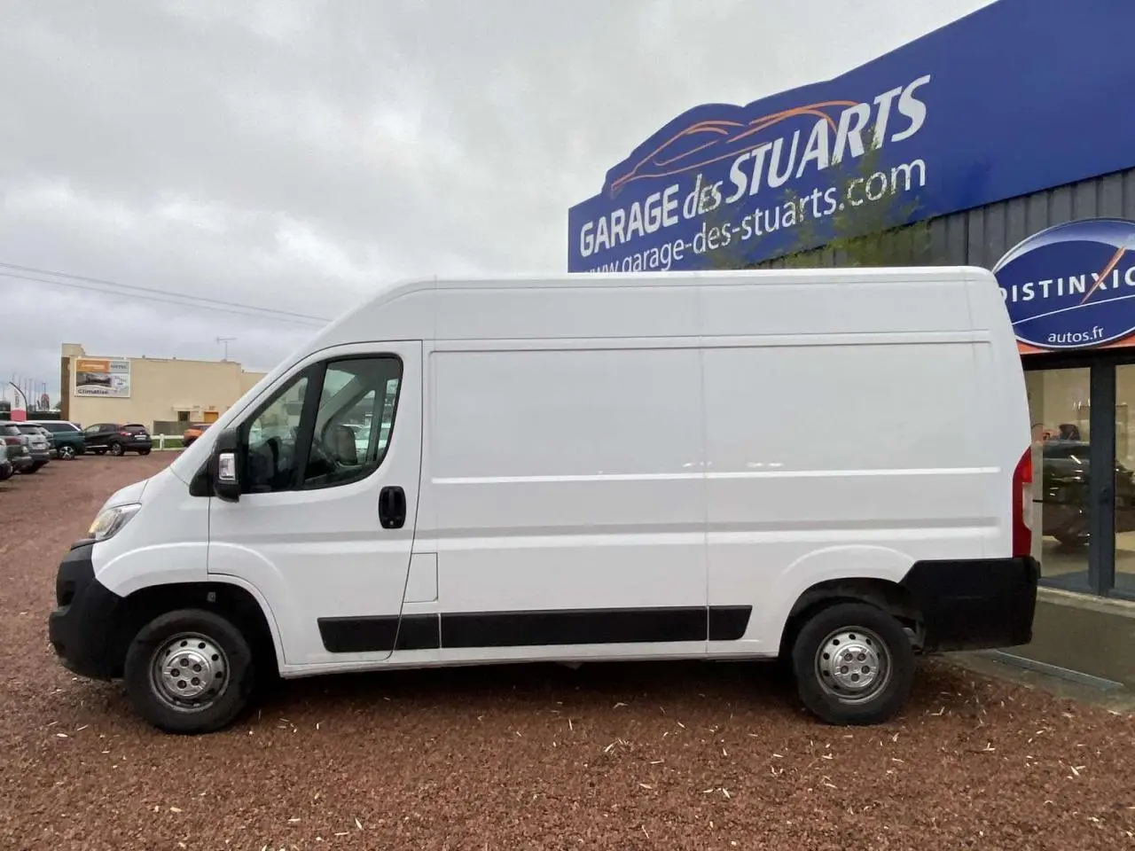 Vue de profil côté gauche d'un fourgon blanc Opel Movano 3.5T L2H2 stationné devant un garage.