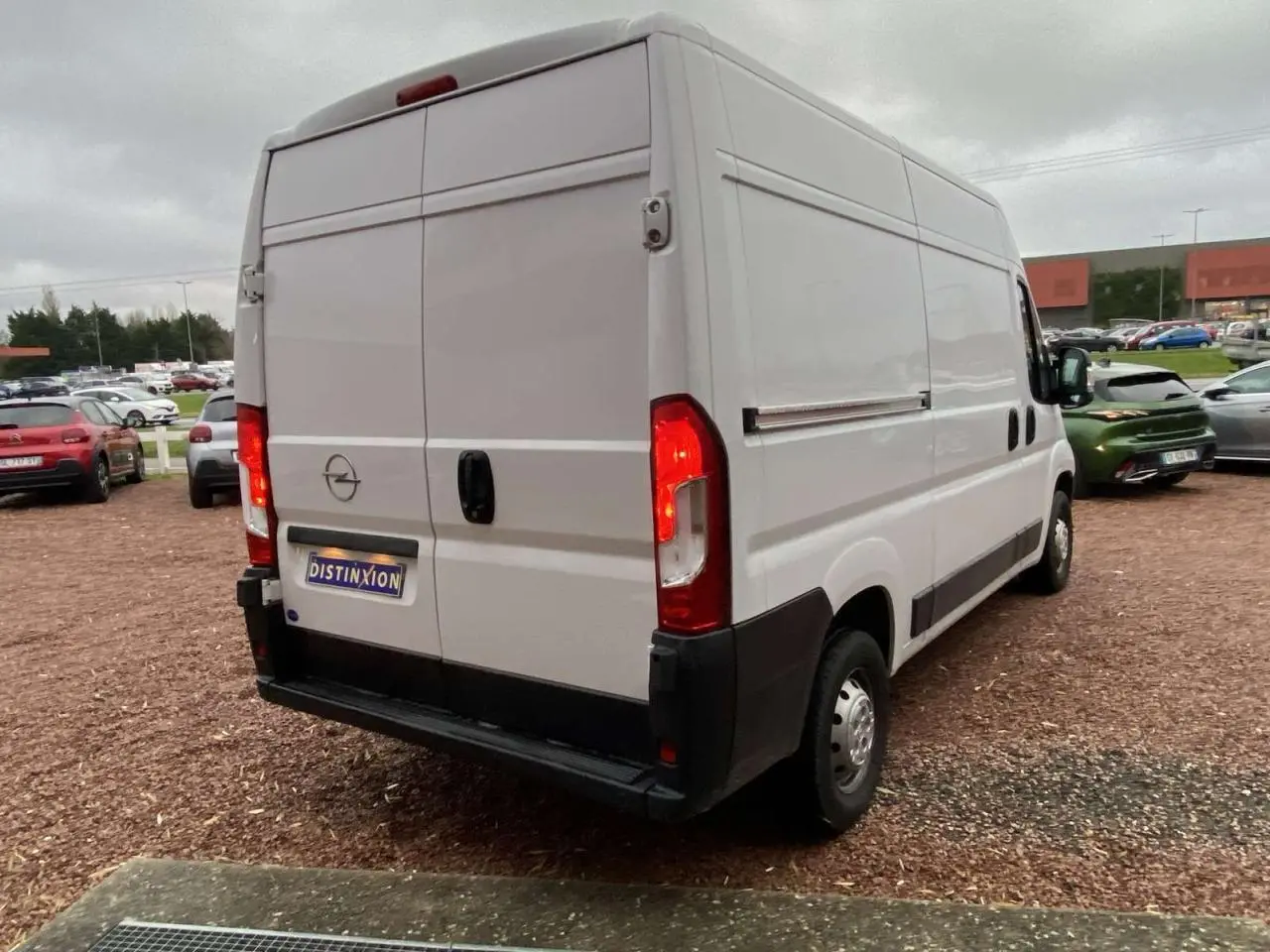 Vue 3/4 arrière droite d’un Opel Movano Fourgon blanc 2022 avec feux arrière allumés sur parking.