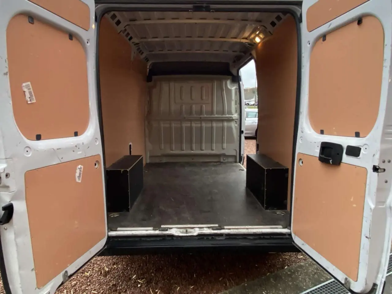 Vue arrière ouverte du fourgon blanc Opel Movano 2022, montrant l'intérieur avec plancher bois et panneaux latéraux beiges.