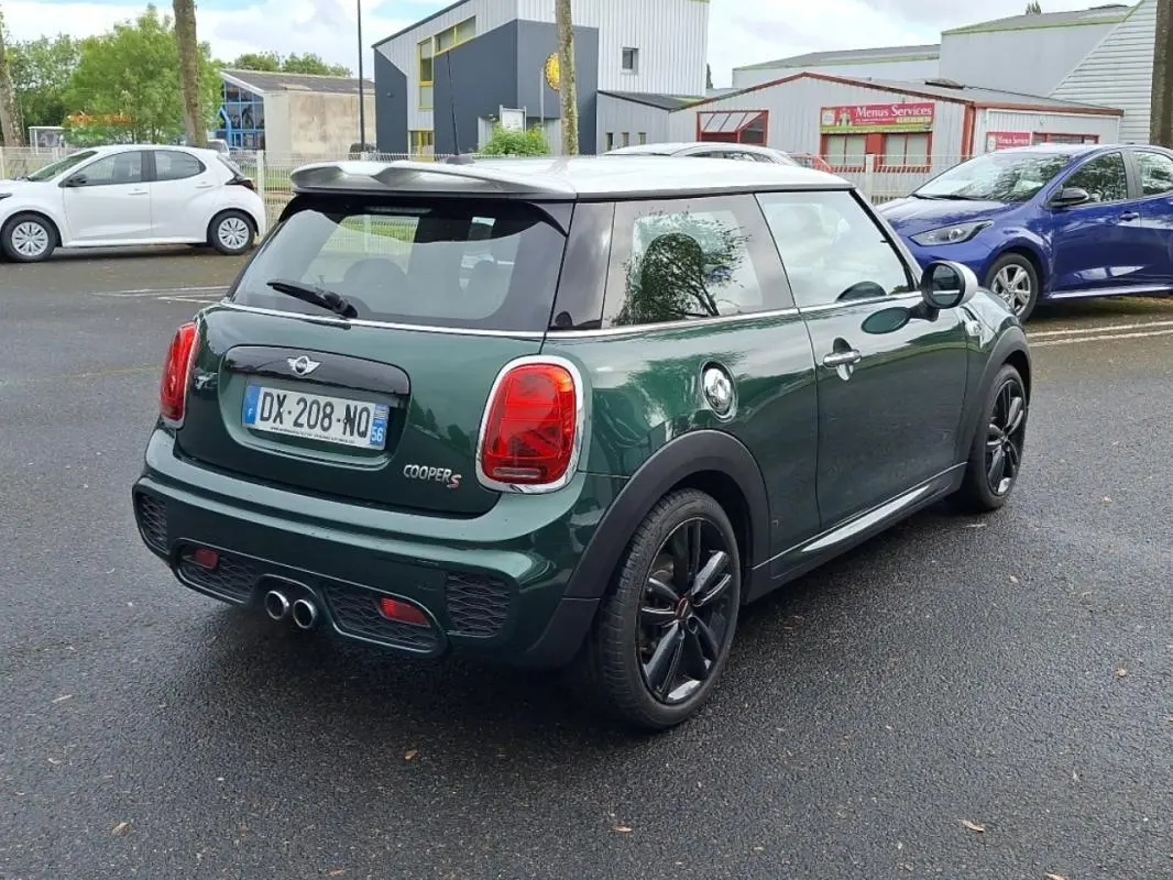 Vue 3/4 arrière d'une MINI Cooper S finition John Work verte avec toit blanc et jantes noires sur parking extérieur.