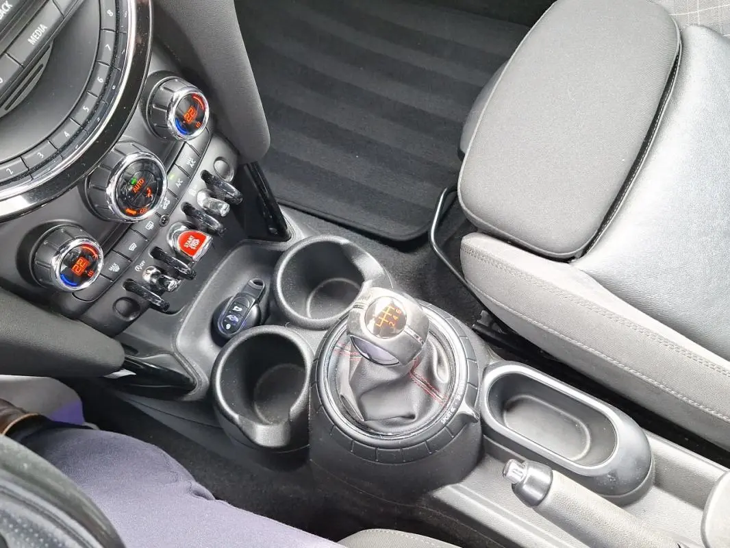 Vue intérieure centrée sur la console centrale et levier de vitesse manuel de la MINI S John Cooper Works 2015, sièges gris.