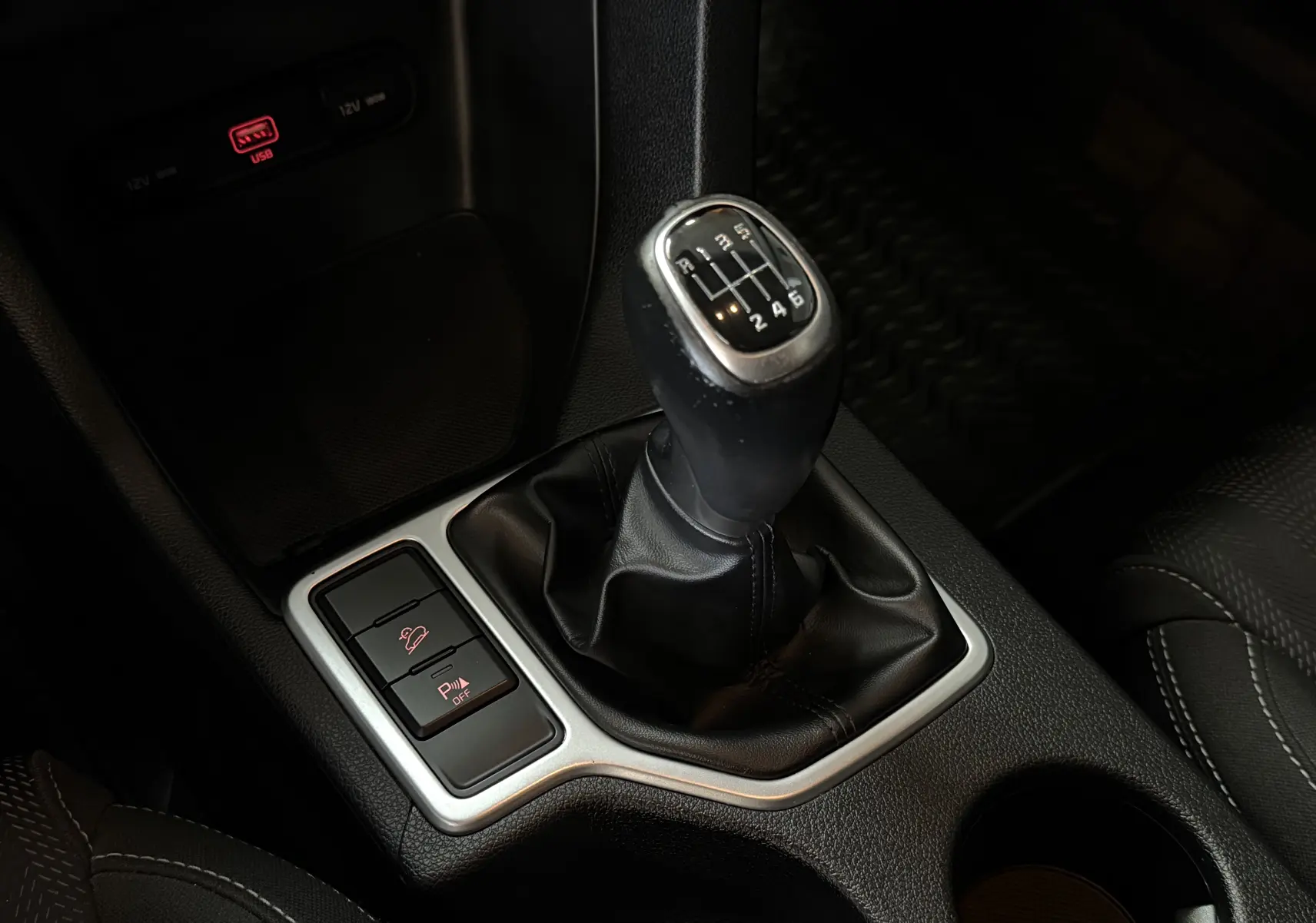 Gros plan sur le levier de vitesse manuel noir du KIA Sportage gris 2019 avec boutons de contrôle à proximité.