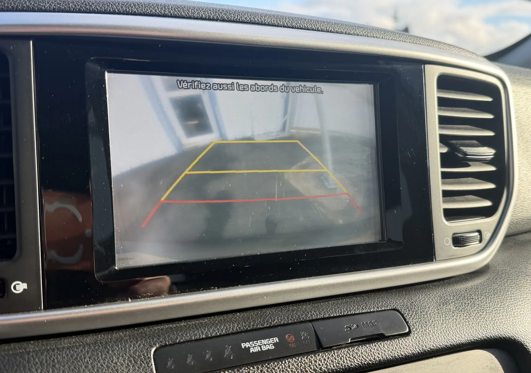 Écran de caméra de recul affichant les lignes de guidage dans un KIA Sportage gris, vue intérieure du tableau de bord.