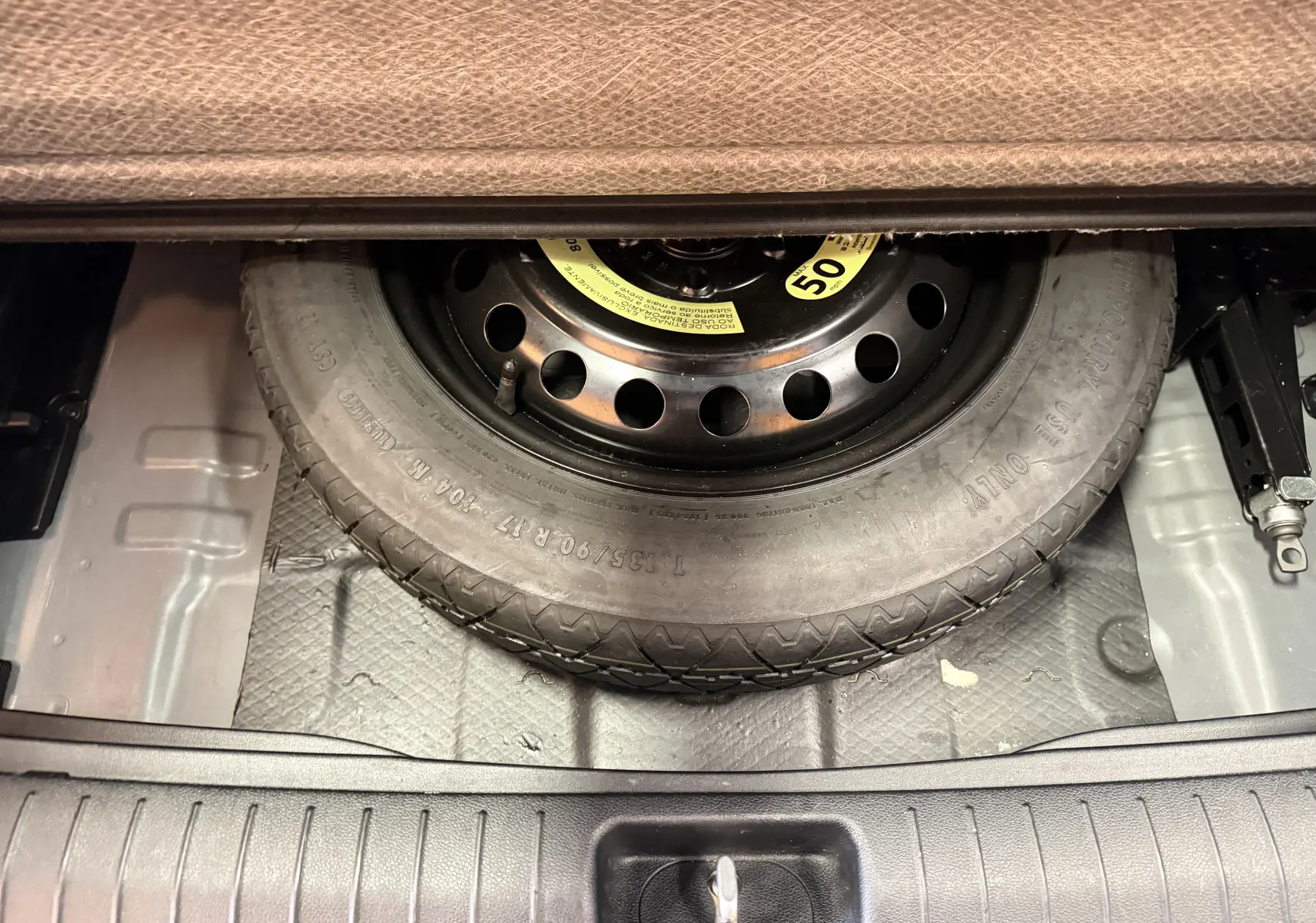 Vue rapprochée du coffre du KIA Sportage 2019 montrant la roue de secours noire sous la moquette grise.
