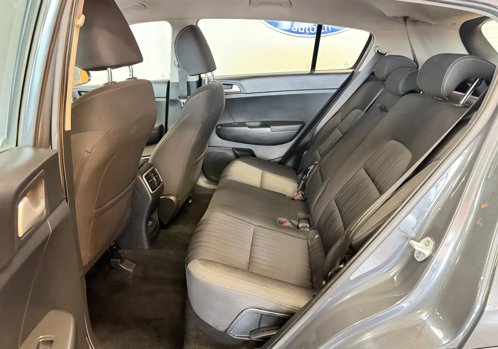 Vue intérieure côté gauche montrant la banquette arrière noire et les sièges avant d’un KIA Sportage gris 2019.