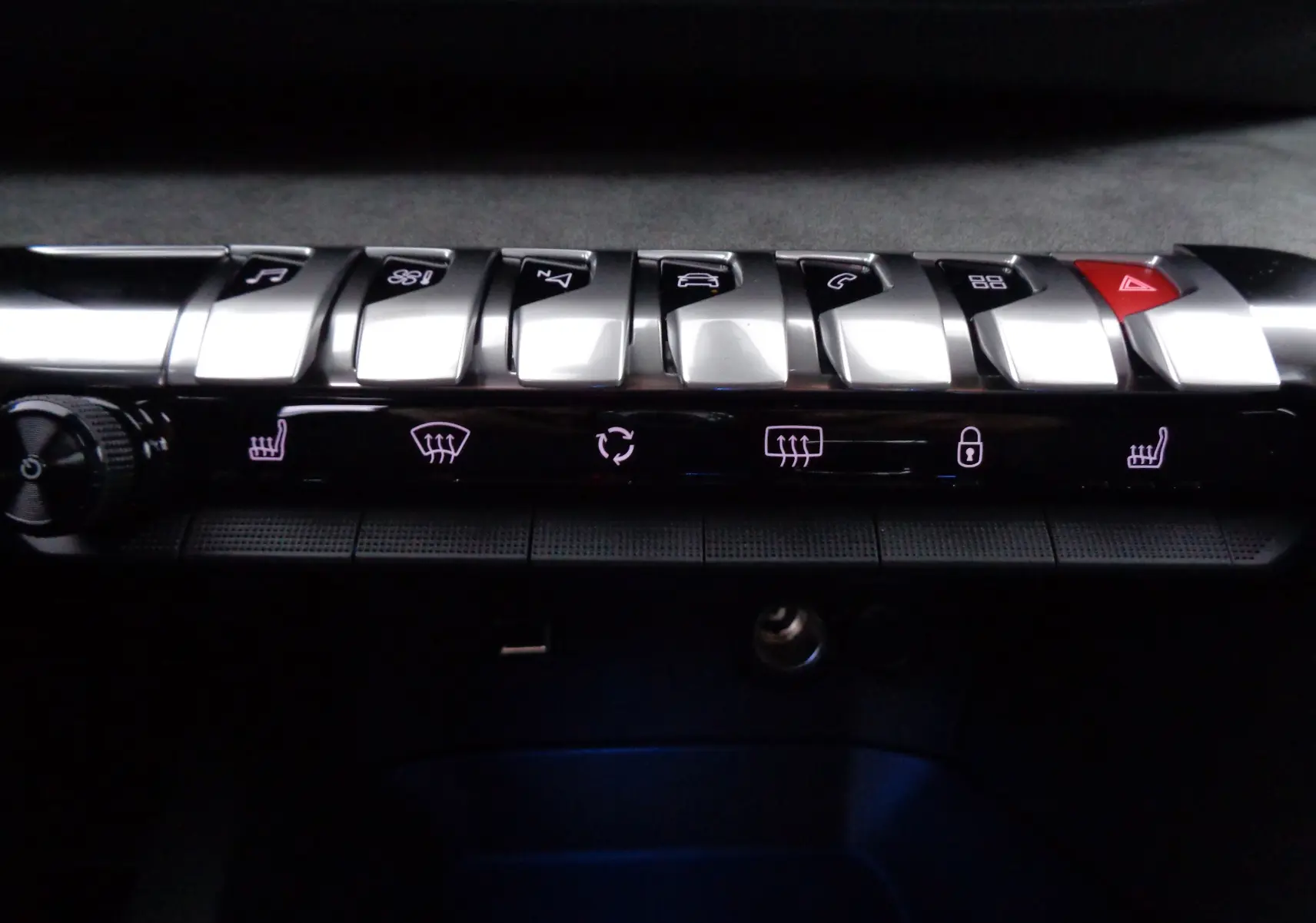 Gros plan sur la rangée de boutons argentés et noirs du tableau de bord du Peugeot 5008 gris platinium, avec commandes éclairées.