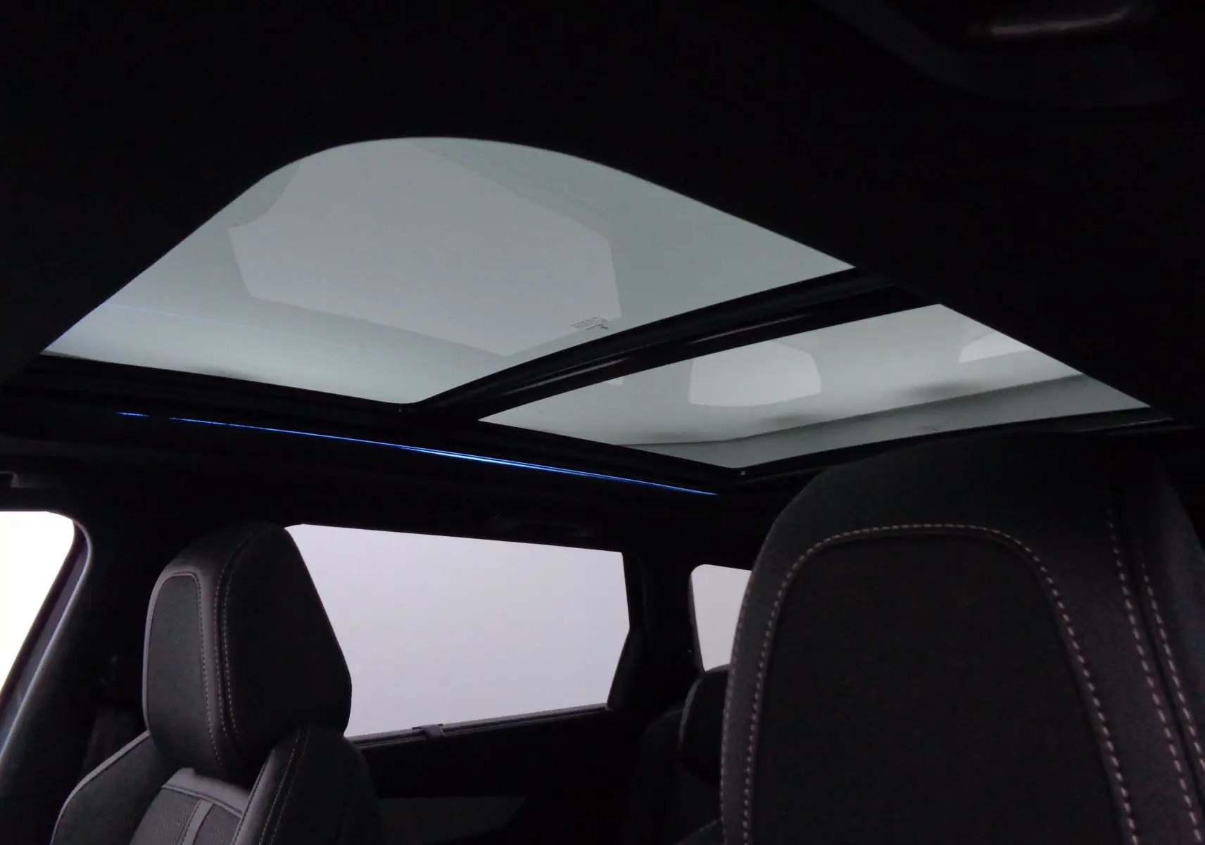 Vue intérieure du Peugeot 5008 GT 2023 montrant le toit panoramique et les sièges avant en cuir noir avec surpiqûres contrastées.