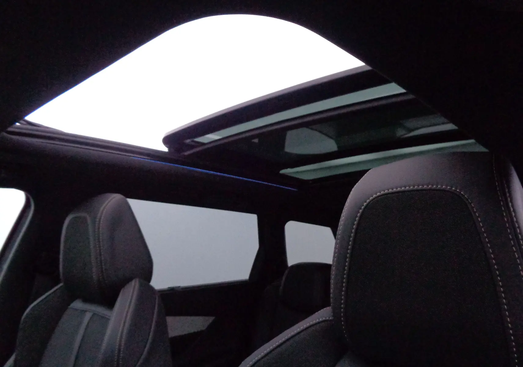 Vue intérieure du Peugeot 5008 2023 montrant les sièges avant en cuir noir et le toit panoramique ouvert.