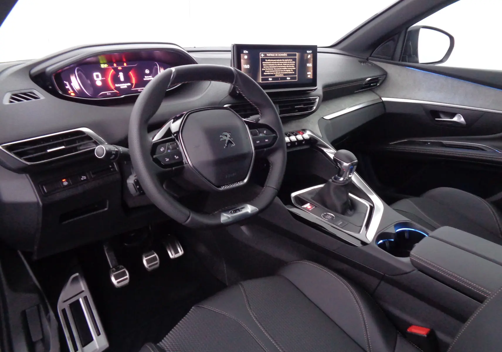 Intérieur avant droit du Peugeot 5008 gris platinium 2023, volant compact, écran tactile et levier de vitesse manuel visibles.