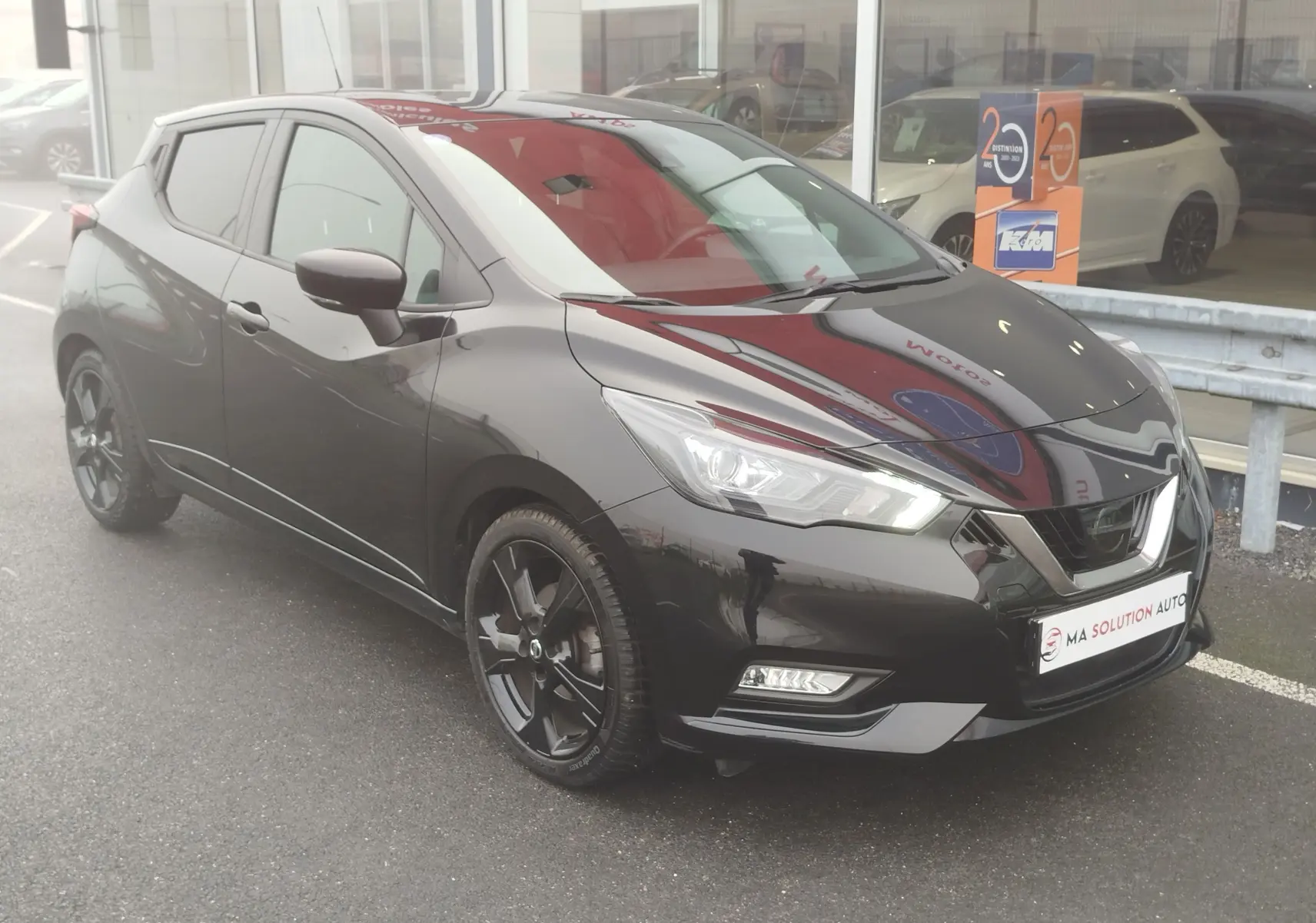 Nissan Micra 2022 noir obscur vue 3/4 avant droit avec jantes noires et phares LED allumés.