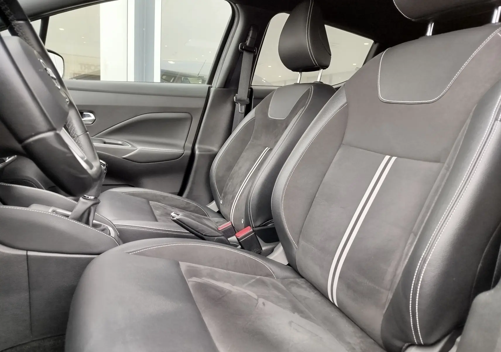 Intérieur de la Nissan Micra 2022 vu côté conducteur, sièges noirs en cuir et alcantara avec surpiqûres blanches et bandes grises.