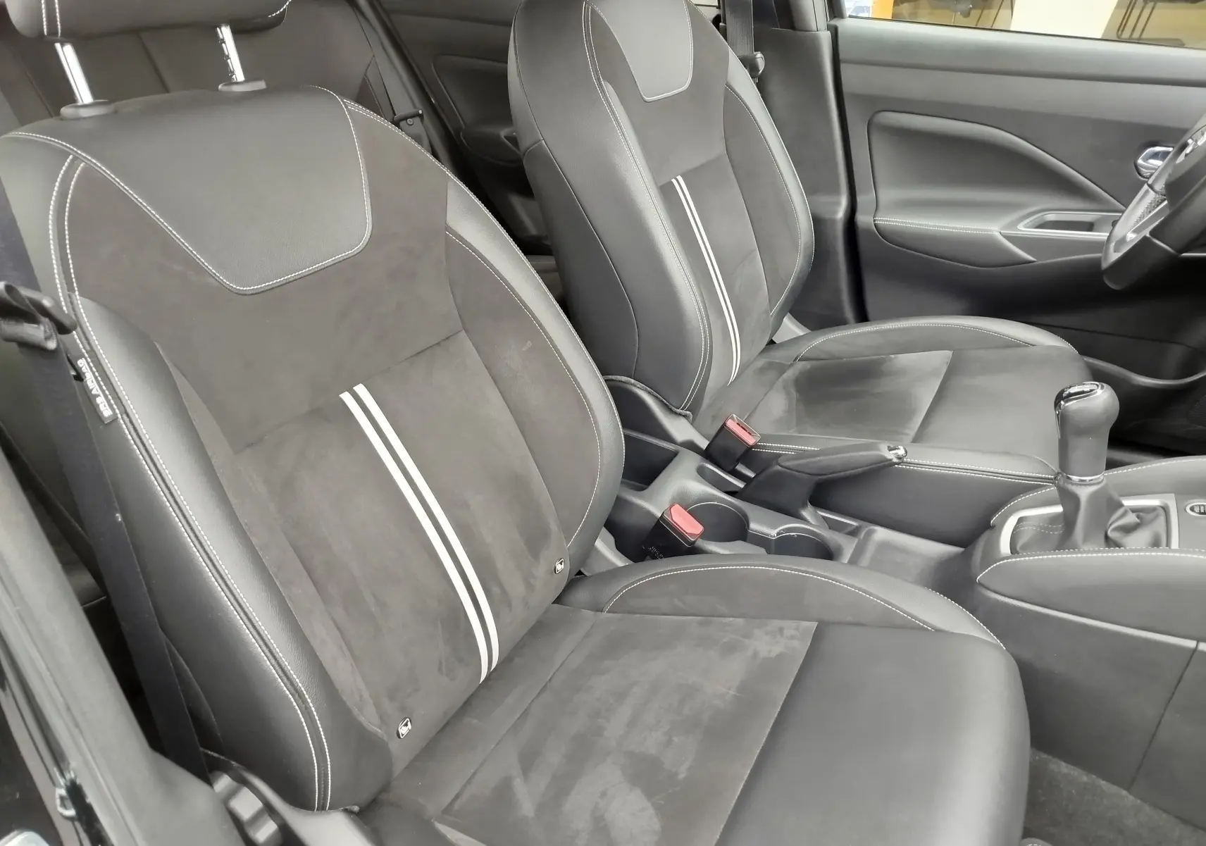 Vue intérieure côté conducteur de la Nissan Micra 2022, sièges noirs en cuir et alcantara avec bandes blanches centrales.