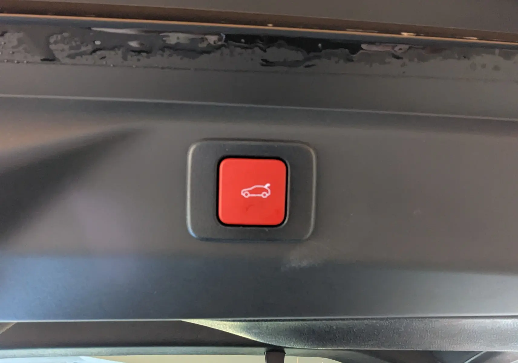 Bouton rouge d'ouverture électrique du hayon sur le coffre intérieur d'un Peugeot 3008 bleu Ingaro hybride.