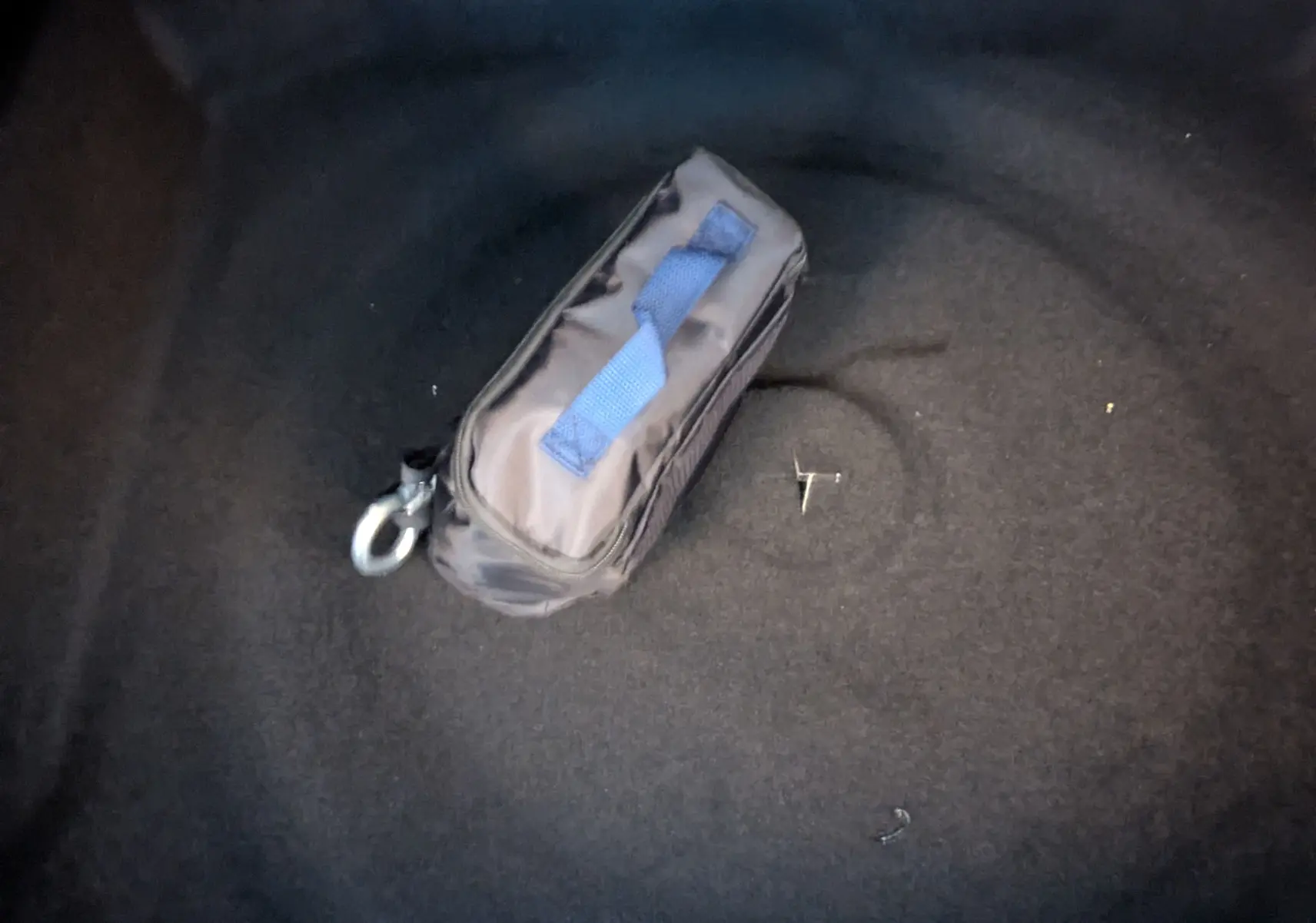 Gros plan sur un sac de secours noir avec poignée bleue posé dans le coffre d’un véhicule.
